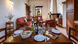 A dining area with a wooden table set for two, surrounded by red patterned sofas, a small side table with a vase, and a view into a kitchen area. - Flat on a Farm With Swimming Pool and Many Activities (Sant'Angelo in Vado)