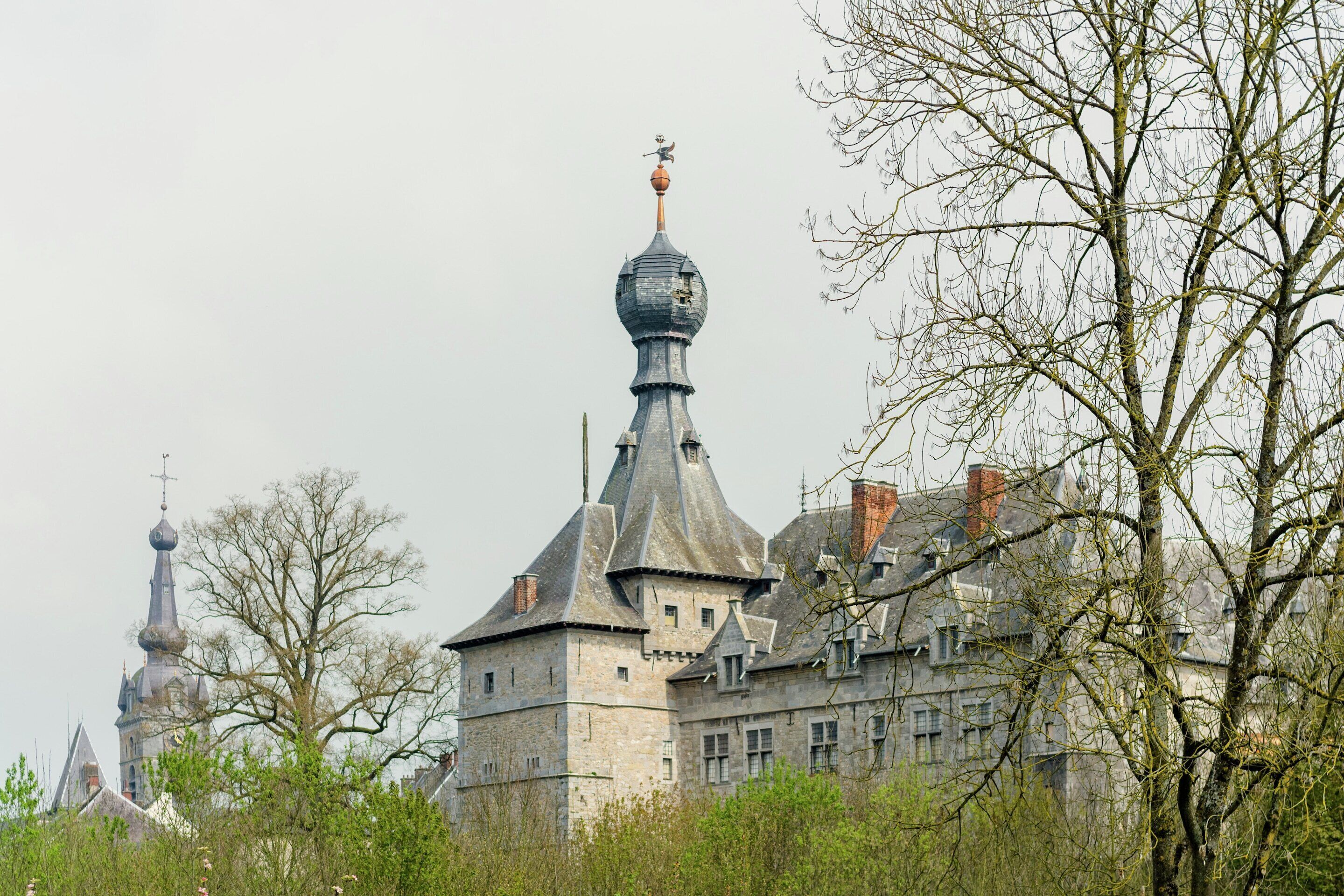 A historic building with a prominent tower and multiple spires, surrounded by trees.