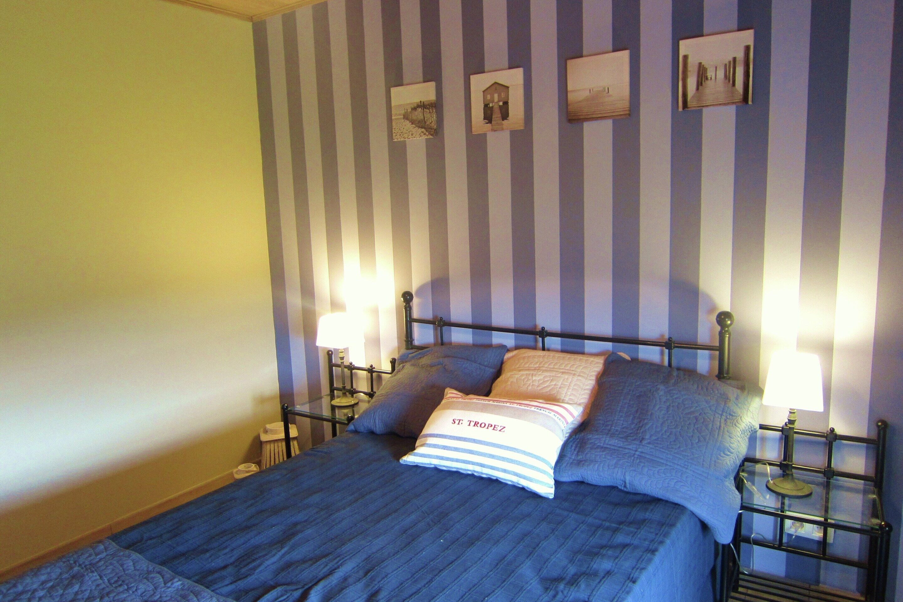Ein Bett mit blauer Bettdecke, zwei Kissen und einem Nachttisch mit Lampe.