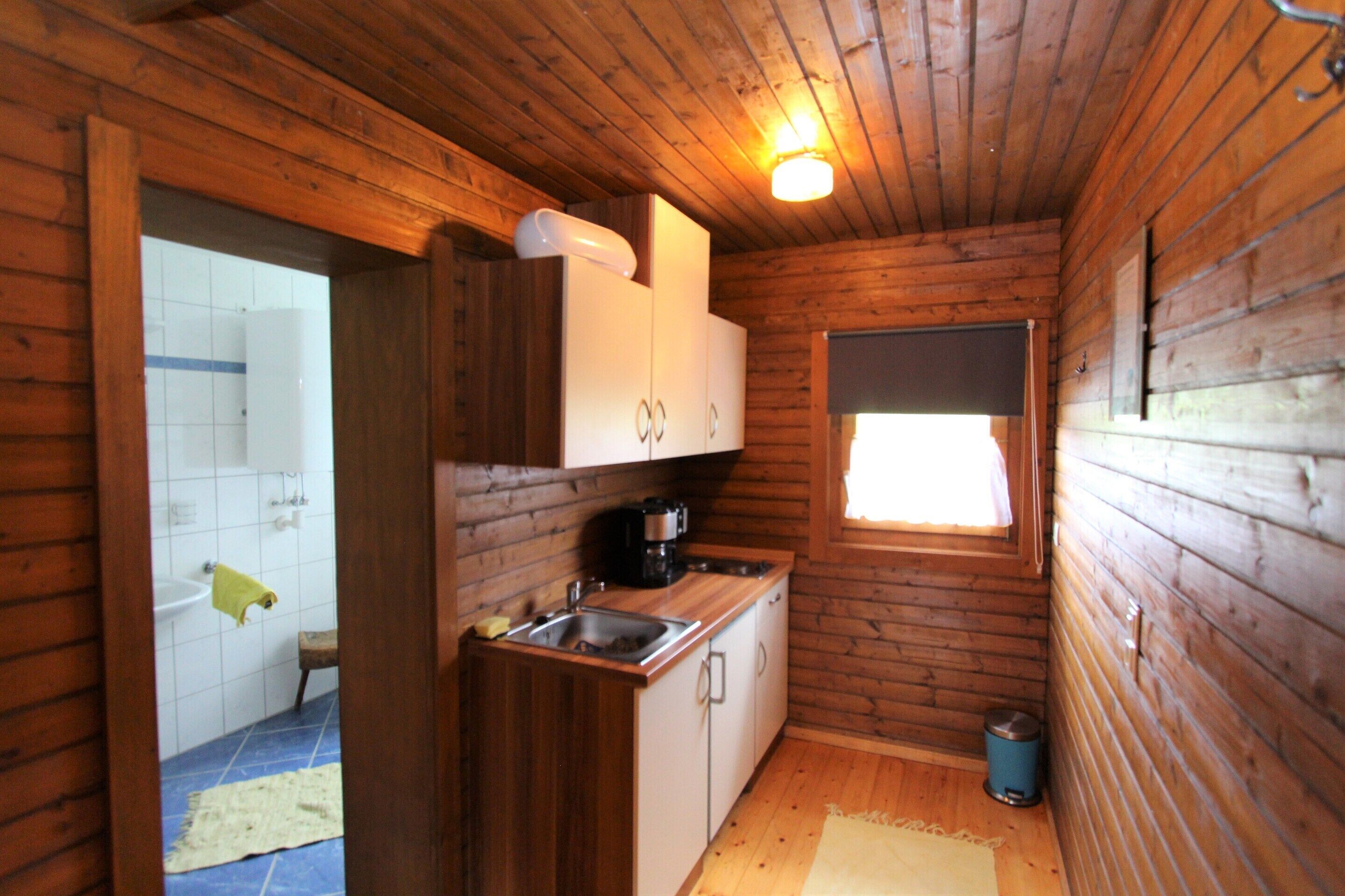 Een kleine keuken met houten wanden, een spoelbak, kastjes, een raam en een afvalbak.