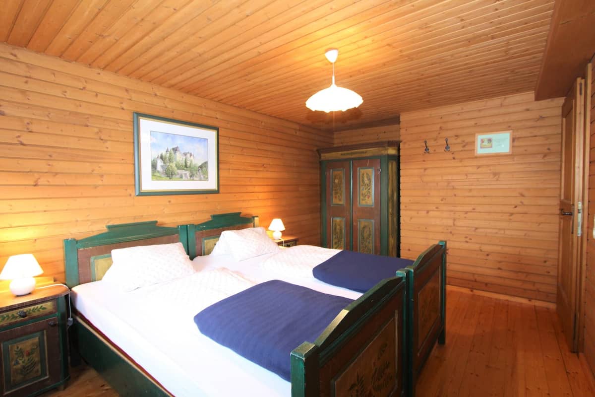 A wooden-paneled room with a double bed, a nightstand with a lamp, and a framed picture on the wall.