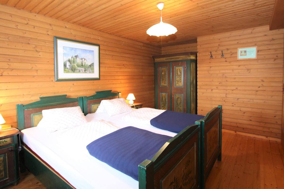 A wooden-paneled room with a bed, a nightstand, a lamp, and a framed picture on the wall.