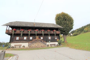 A wooden building with a balcony, a staircase, and a tree in the background.