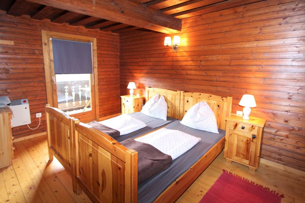 A wooden cabin room with a bed, two bedside tables, a window, and a heater.