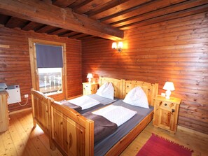 A wooden cabin room with a bed, two bedside tables, a window, and a heater. - Characterful old Farmhouse With 4 Apartments in Fresach / Carinthia With Garden (Fresach)