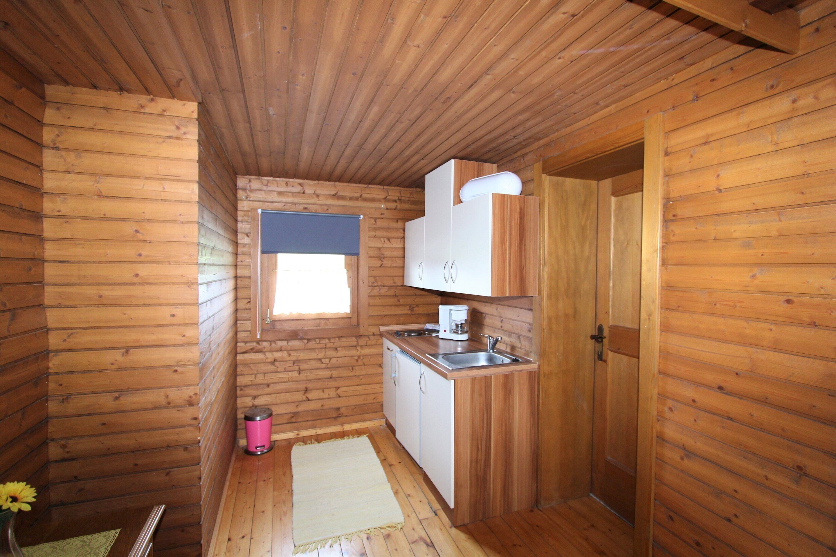 Una cabaña de madera pequeña y acogedora con kitchenette, un ventanal y una puerta.
