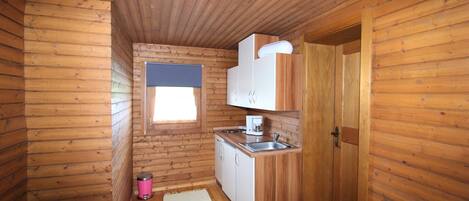 Una cabaña de madera pequeña y acogedora con kitchenette, un ventanal y una puerta.