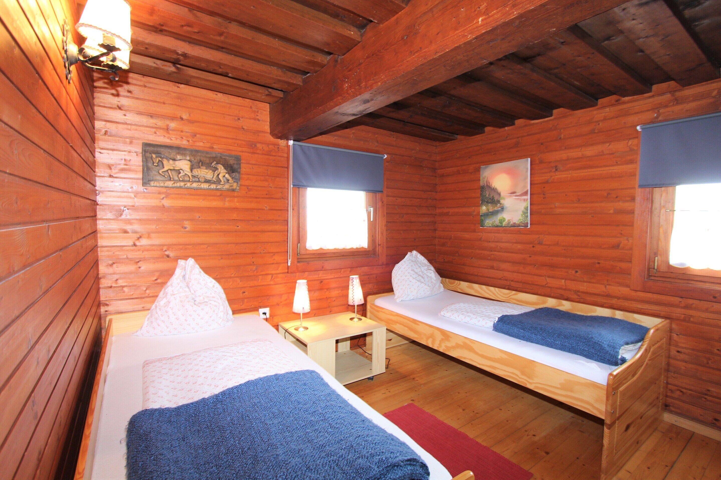 A wooden cabin with two single beds, a small table, and a bench.