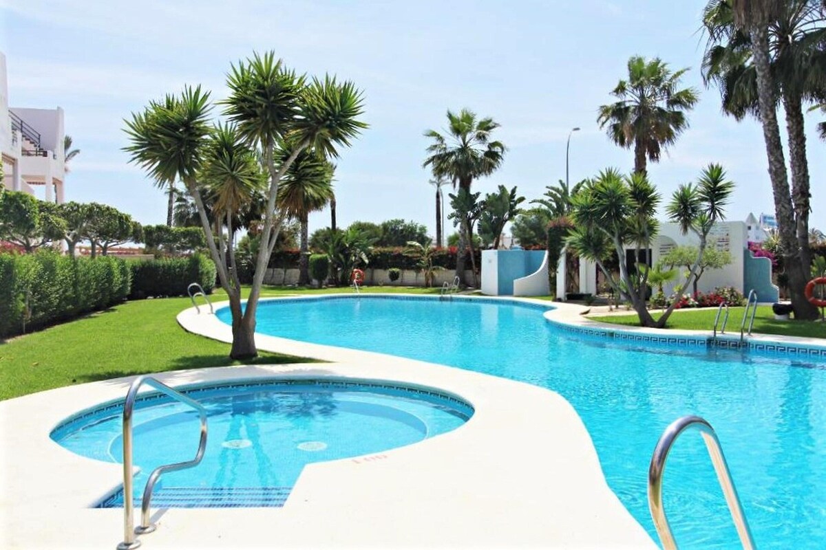 Una piscina de borde curvo, rodeada de palmeras y un césped bien cuidado.