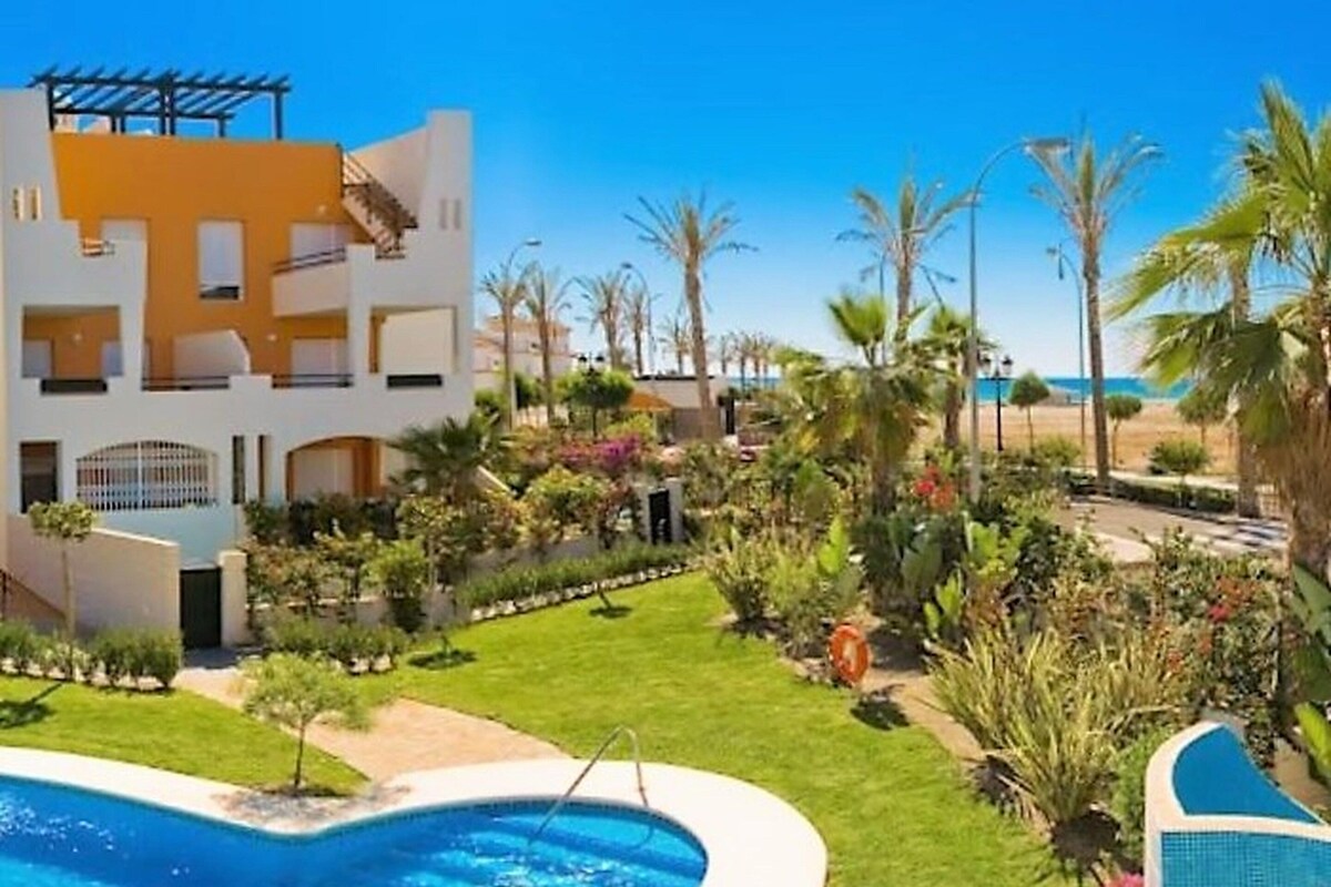 Un hotel moderno con piscina, abundante vegetación y vistas despejadas a la playa.