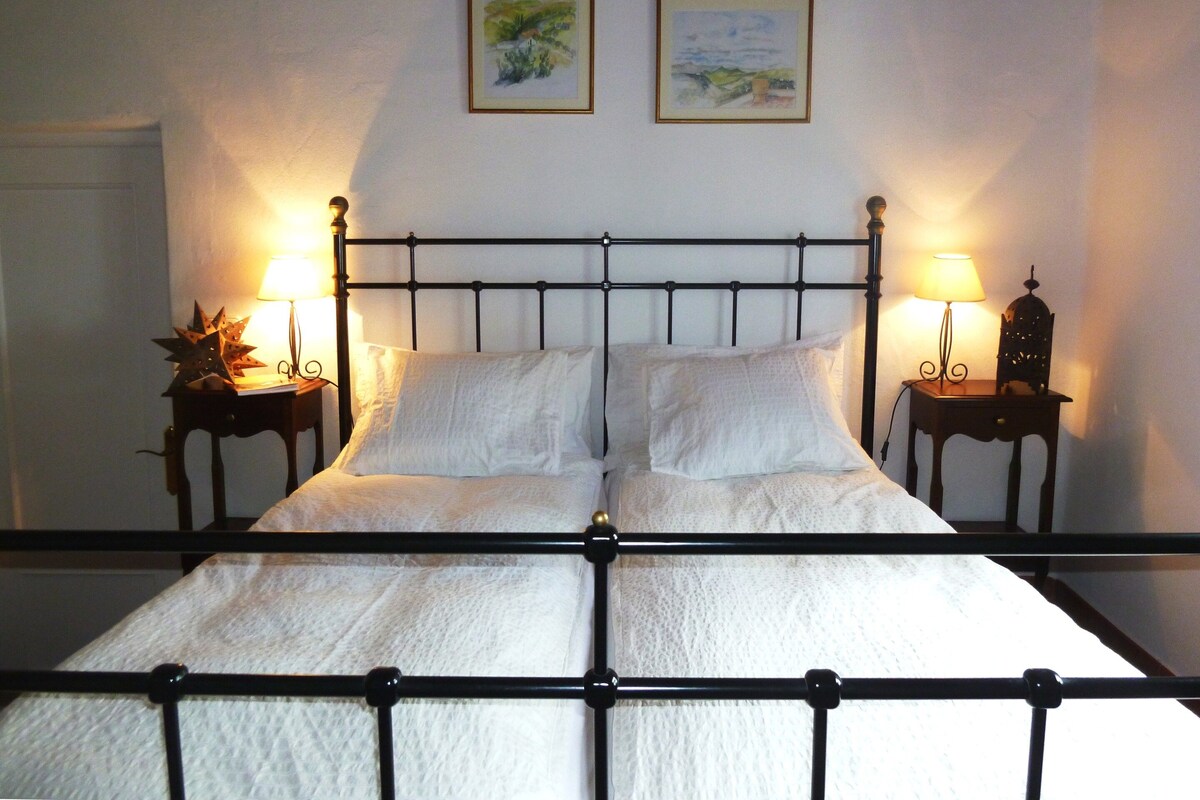 A bed with a metal frame, two bedside tables with lamps, and two framed pictures on the wall.
