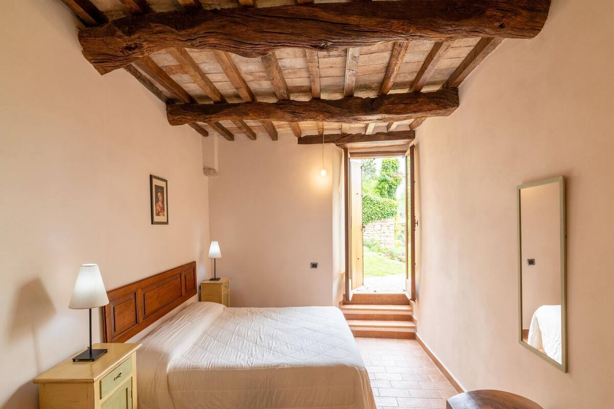 Ein Schlafzimmer mit Holzboden, einem Bett mit weißer Bettdecke, einem Nachttisch mit Lampe und einem kleinen Schrank.