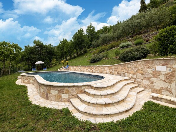 Une piscine avec des marches en pierre et un fauteuil de relaxation.