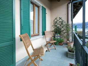 A balcony with two wooden chairs, a potted plant, and a decorative wall piece. - Enticing Apartment in Stresa With Balcony & Lake Views (Stresa)