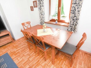 A wooden dining table with six chairs, a vase with flowers, and a window with curtains. - Pleasant Apartment in Ruhpolding With Swimming Pool (Ruhpolding)