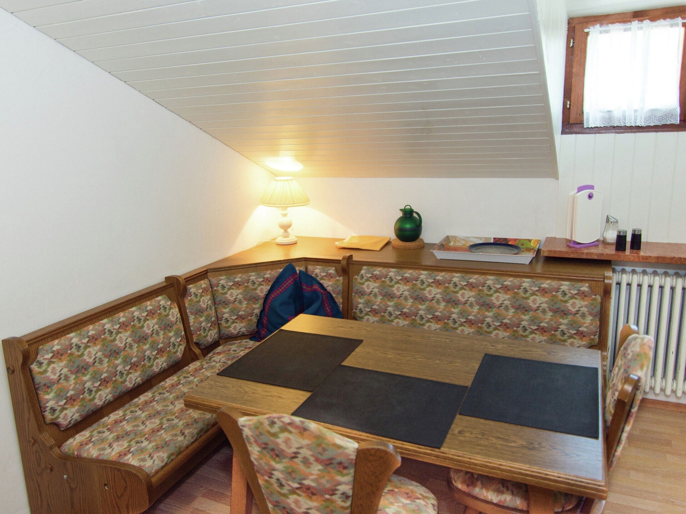 A cozy corner with a wooden table and floral-patterned benches, a lamp, and a radiator.