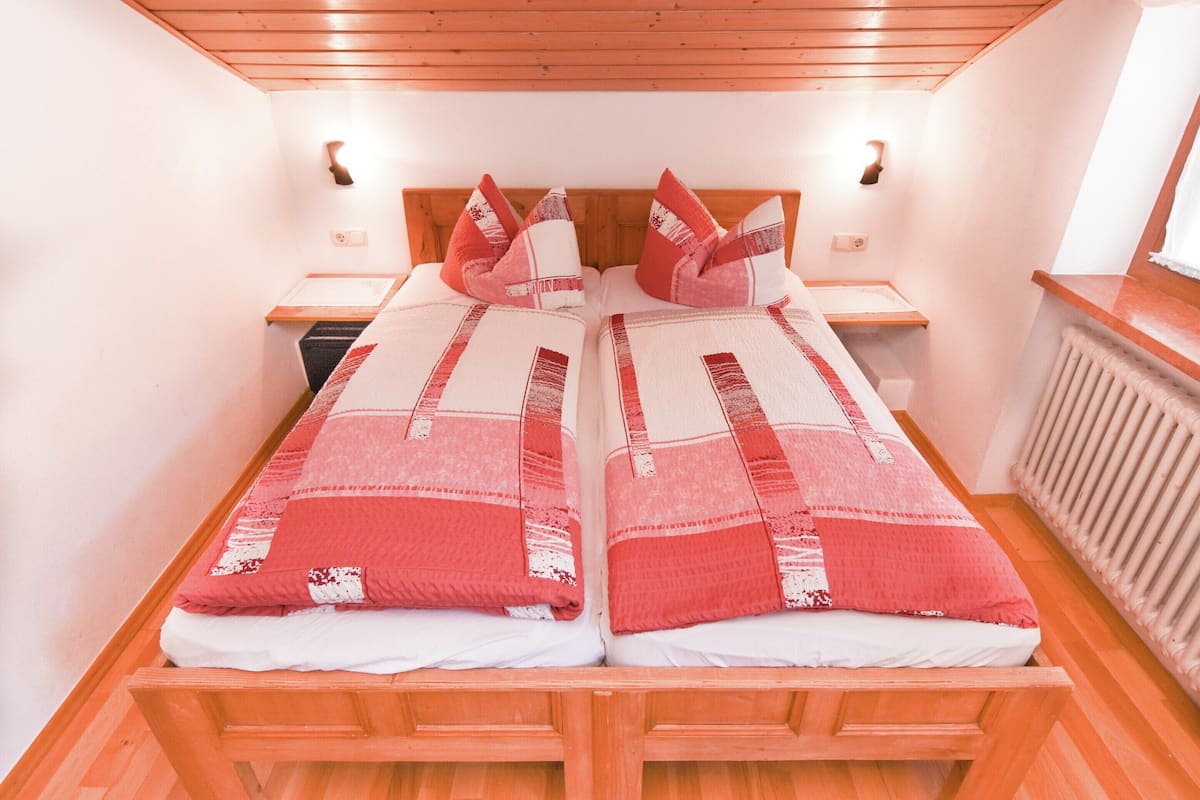 Un lit double avec une couvre-lit à motifs rouges et blancs, une tête de lit en bois, des tables de chevet et un plancher en bois.