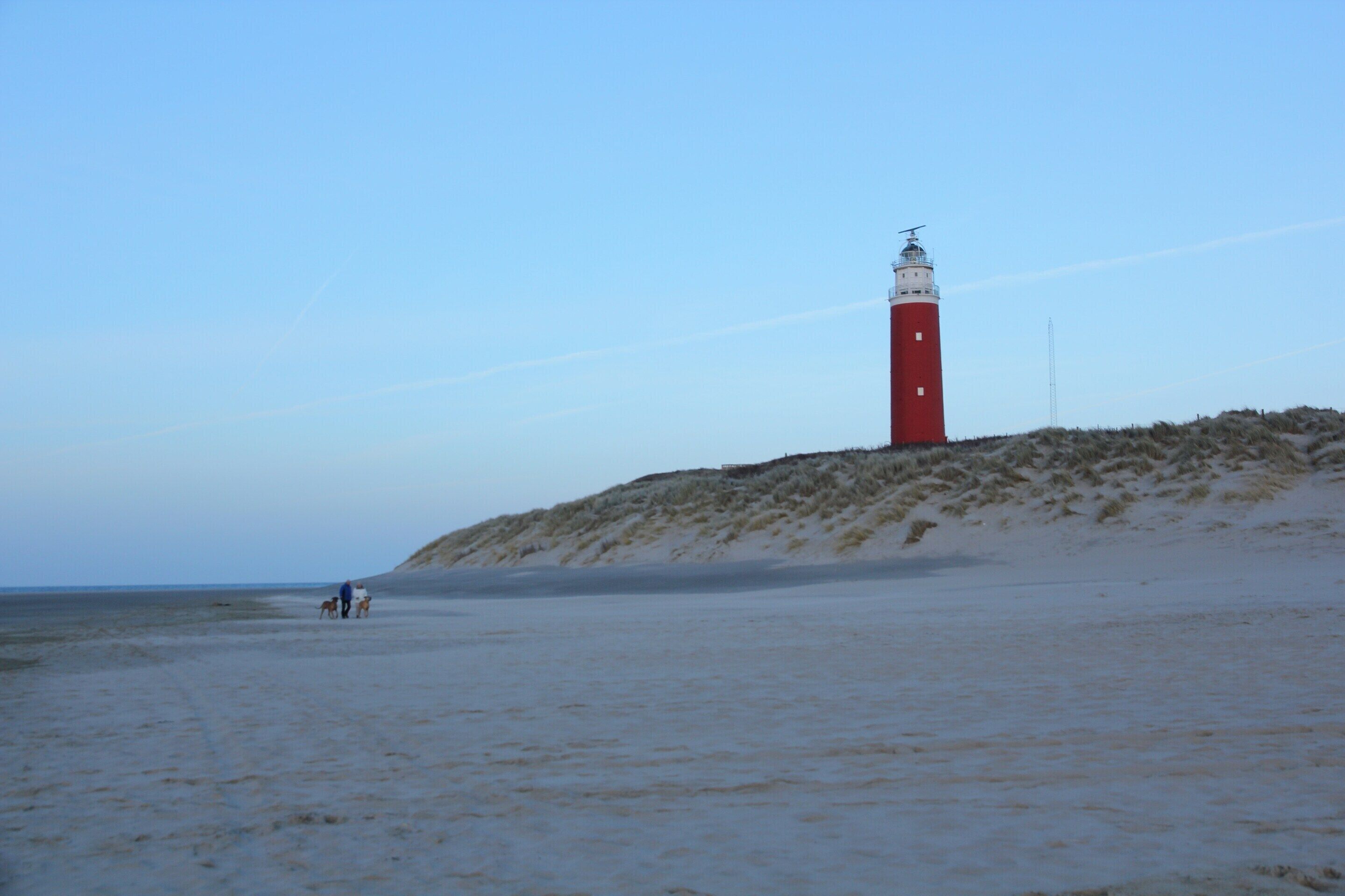 A lighthouse on a sandy beach with a clear sky.