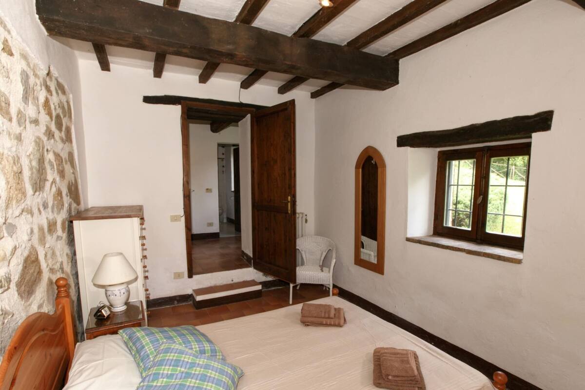 A bedroom with a wooden bed, a stone wall, a window with a view, and a mirror.