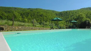 Piscina cristalina con paredes de piedra y sombrillas verdes.