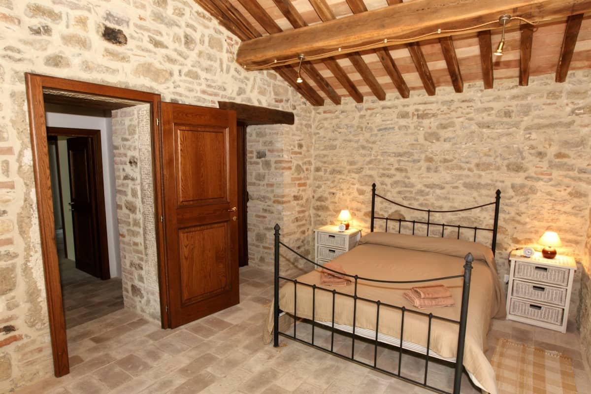 A bedroom with a stone wall, a wooden door, a metal bed frame, and bedside tables with lamps.