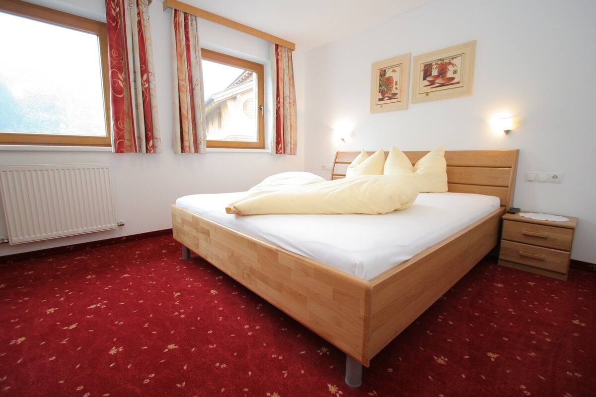 A neatly made bed with white linens and a wooden headboard in a room with a red carpet.