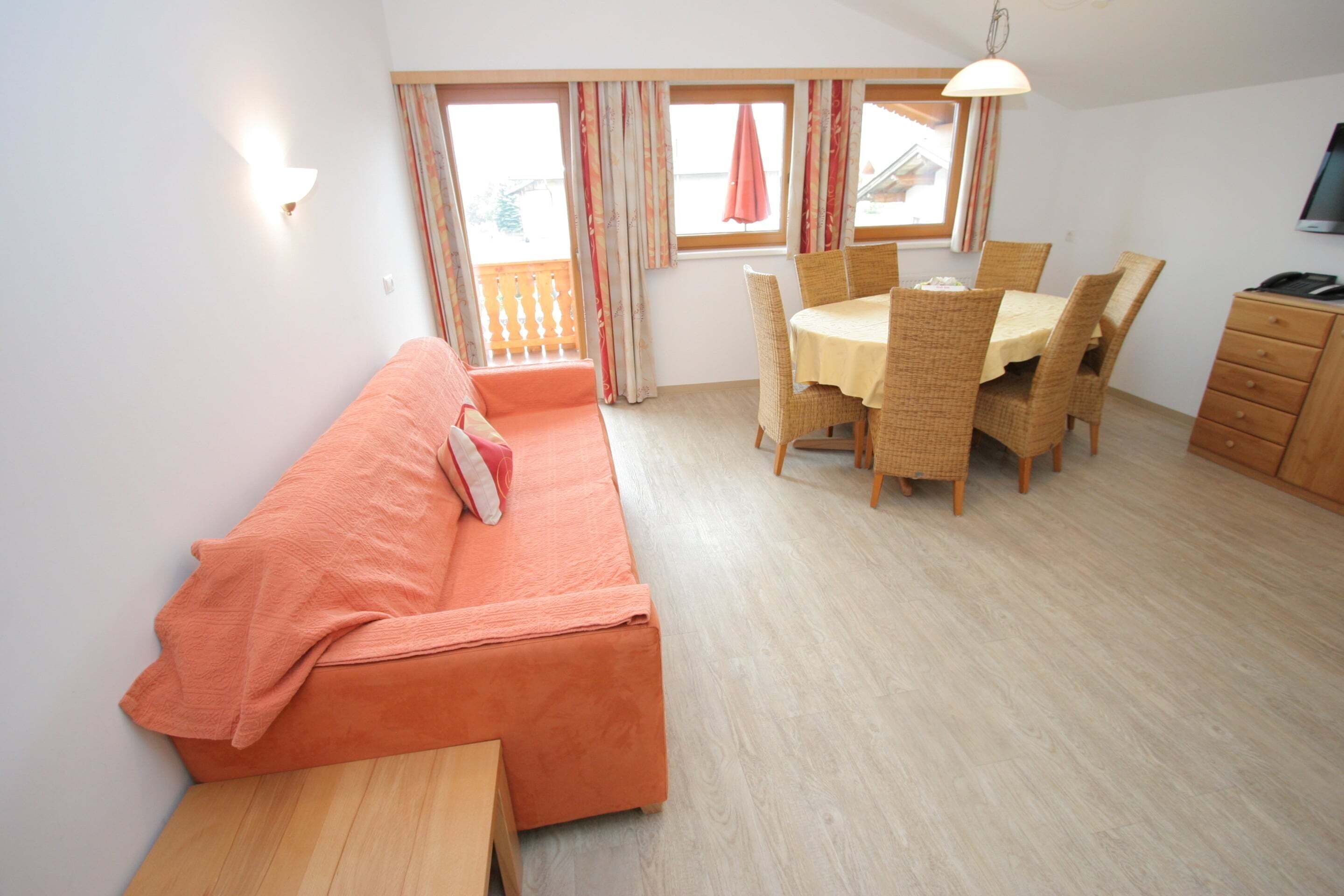 A room with a sofa, a dining table with chairs, a wooden cabinet, and a window with curtains.