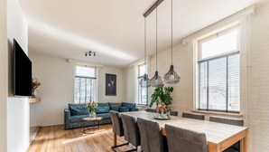 A modern living room with a wooden floor, a sofa, a dining table with chairs, pendant lights, and a TV mounted on the wall. - Spacious Farmhouse in Silvolde With Garden (Silvolde)