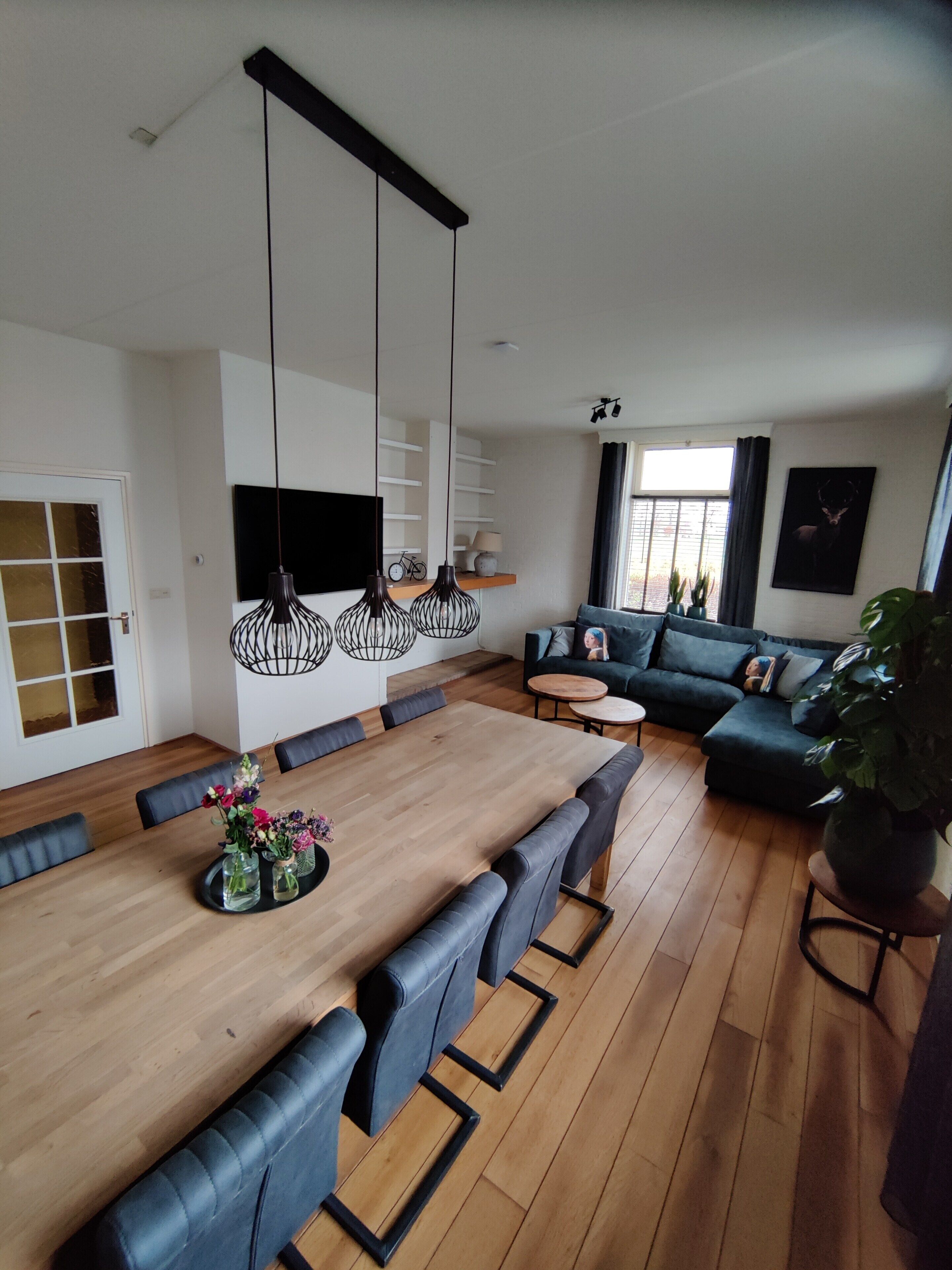 A modern living room with a wooden dining table, black leather sofas, and hanging pendant lights.