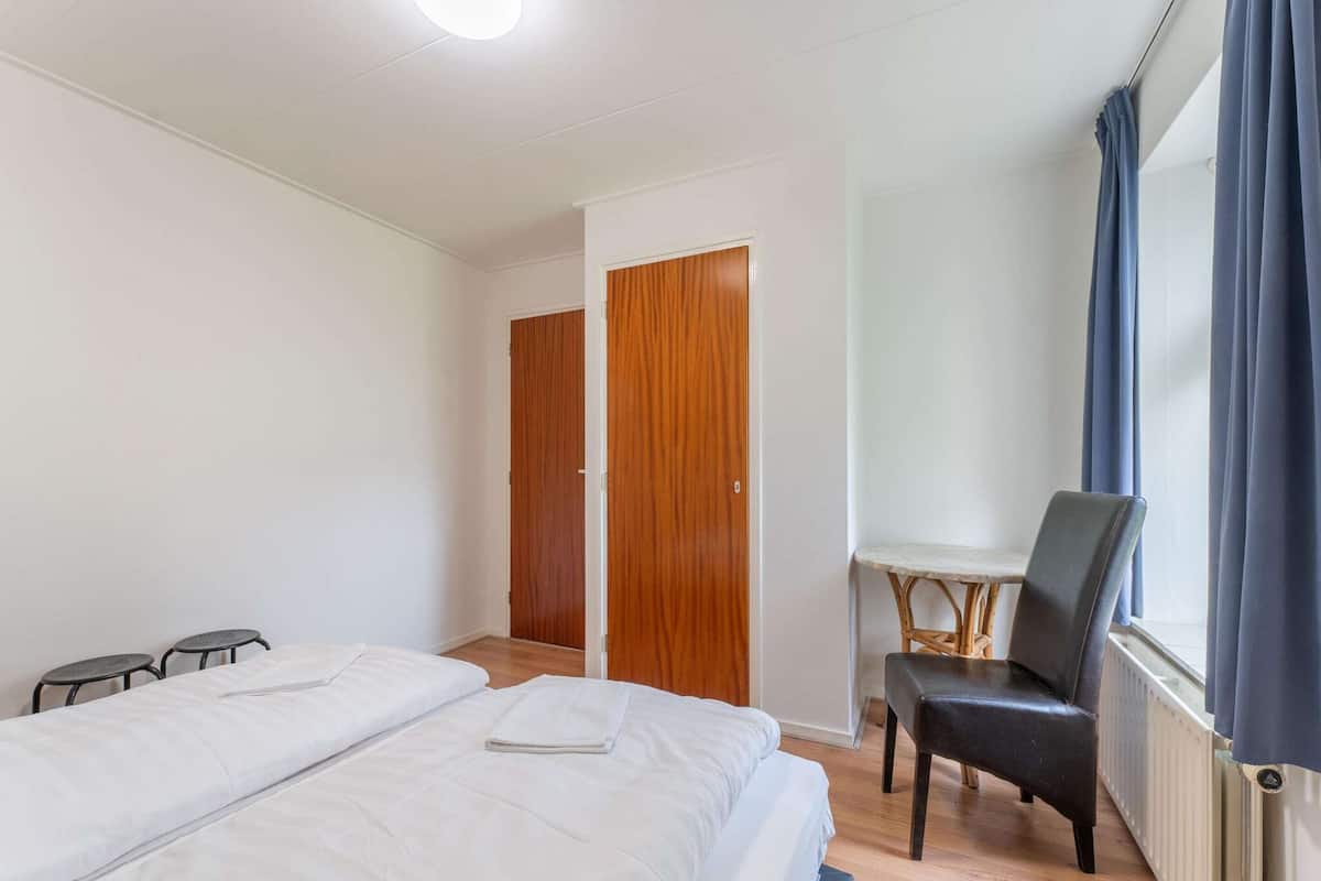 Une chambre d’hôtel avec deux lits, une armoire en bois, une petite table avec une chaise et une fenêtre avec des rideaux.