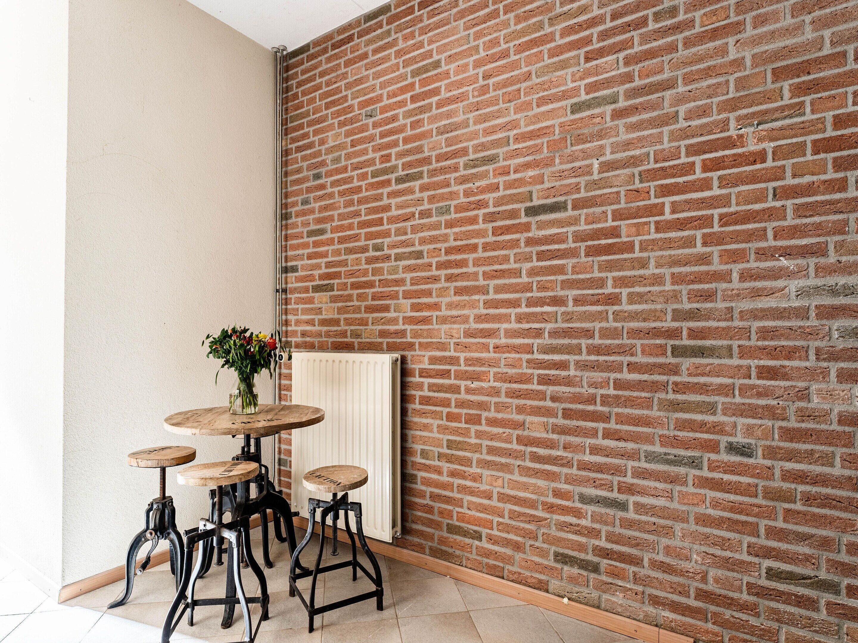 Ein Eckzimmer mit Backsteinwand, Heizkörper und rundem Holztisch mit Hockern.
