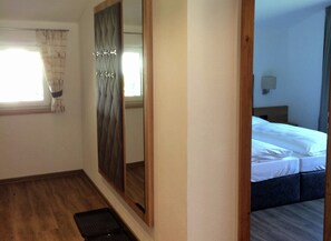 Une chambre d’hôtel avec un grand miroir, un lit recouvert de draps blancs, un plancher en bois et une fenêtre avec des rideaux.