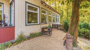 A house with a gravel driveway, a wooden cart with flowers, and a tree in the foreground. - Rustic Apartment With Garden in Bad Harzburg Germany (Bad Harzburg)