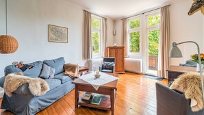 A cozy living room with a blue sofa, a wooden coffee table, and a view of greenery through large windows. - Rustic Apartment With Garden in Bad Harzburg Germany (Bad Harzburg)