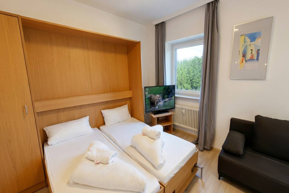 Habitación de hotel con dos camas, televisión, sofá y ventana con cortinas.