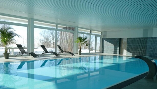 Une piscine intérieure à l’eau d’un bleu limpide, entourée de grandes fenêtres et agrémentée de plantes en pot.
