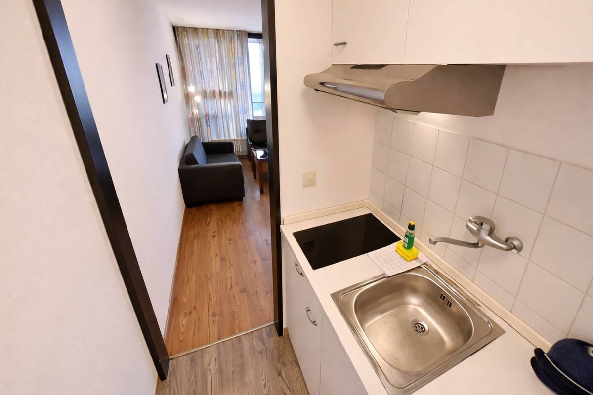 Una cocina compacta con un lavamanos de acero inoxidable, una pequeña encimera y un armario arriba.