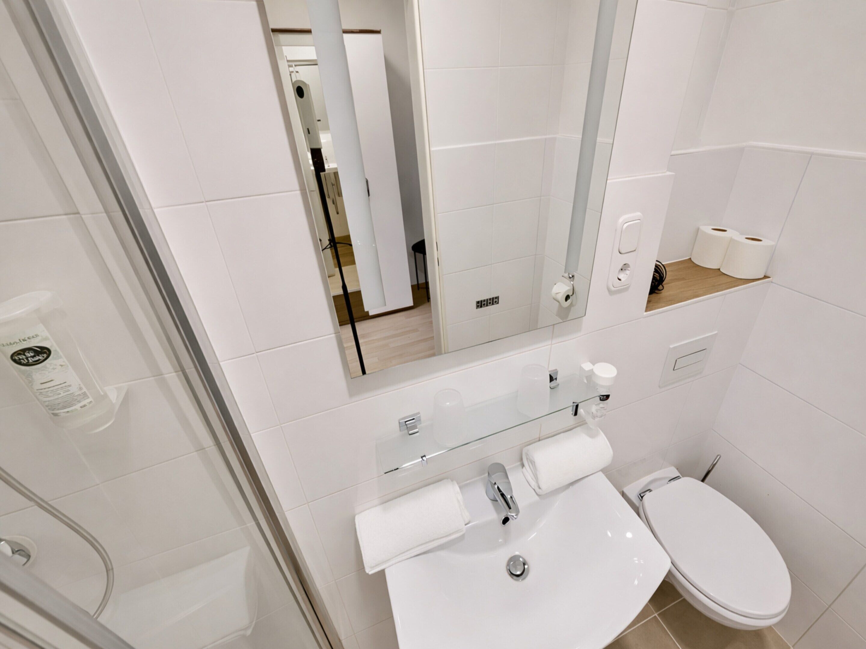 Een moderne badkamer met een douchecabine van glas, een wit wastafelmeubel met spiegel en een toilet.