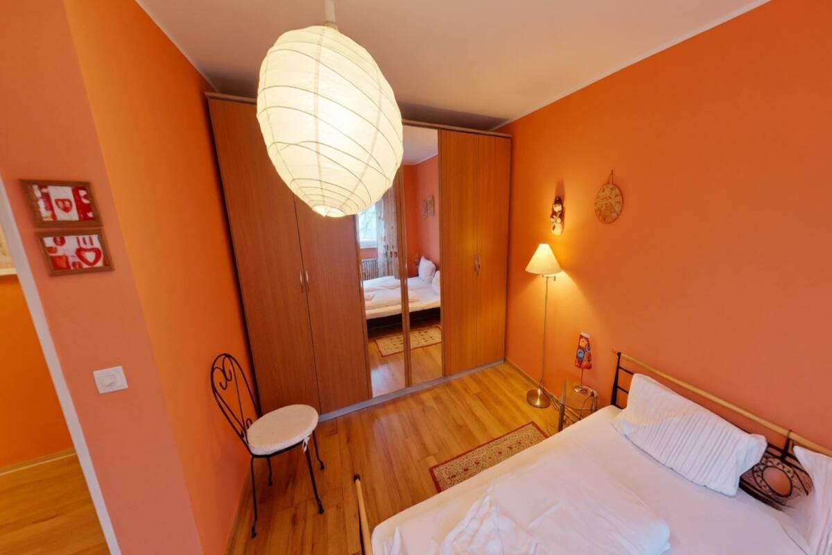 Un dormitorio con cama, una silla, una lámpara de noche, un armario y un espejo.