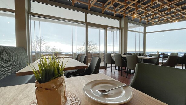A dining area with a table set for two, large windows, and a view of the sky. - Holiday Apartments in Freyung With Sauna & Swimming Pool (Freyung)