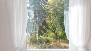 A window with white curtains, a view of a forest with tall trees and a fallen tree. - Spacious Apartment Near Forest in Bad Durrheim (Bad Duerrheim)