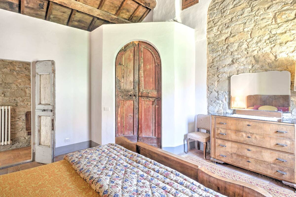 A rustic bedroom with a wooden bed, a stone wall, and a wooden dresser.