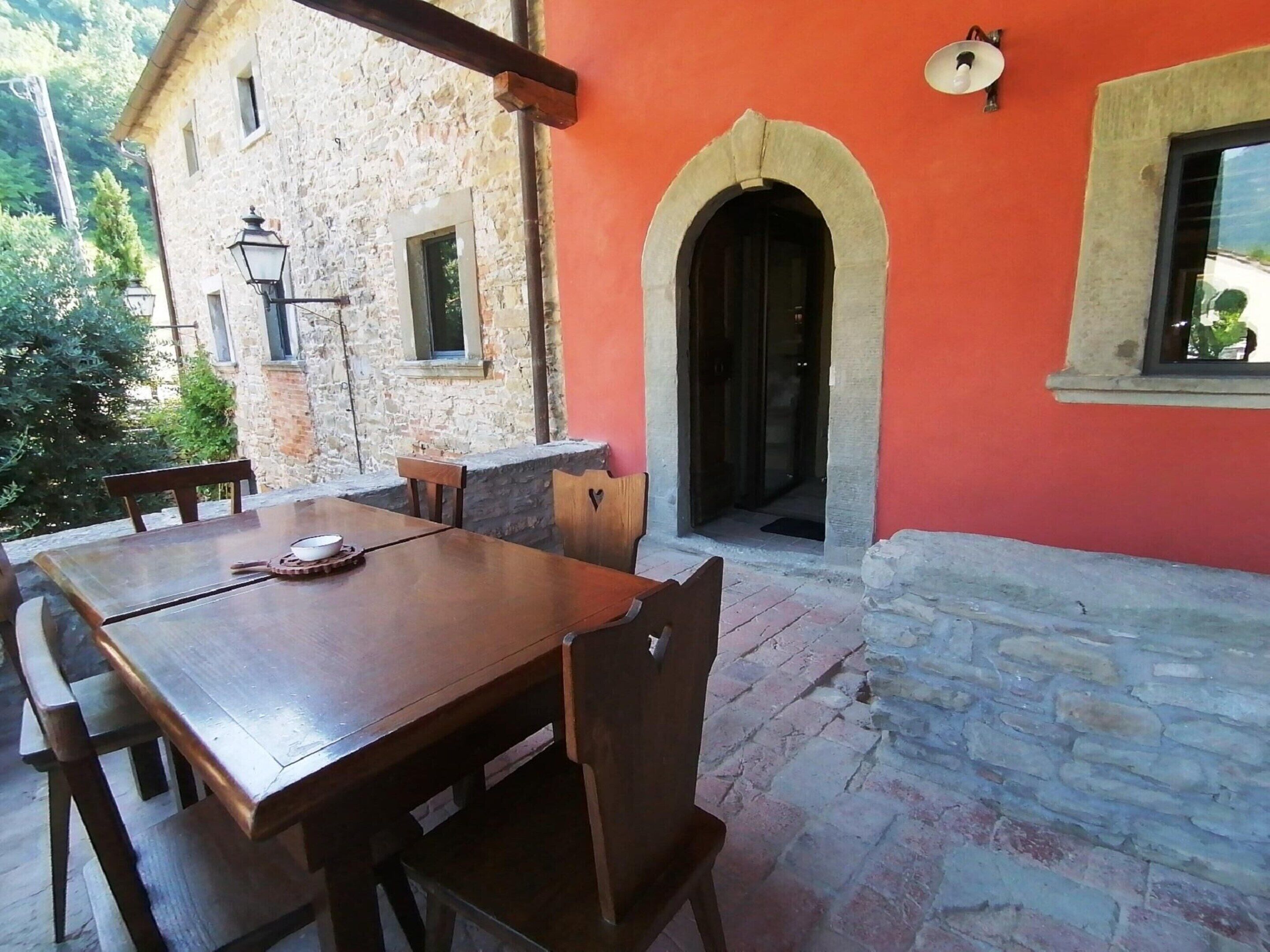 Un edificio de piedra con una mesa y sillas de madera, una pared roja y otra de piedra con una puerta.