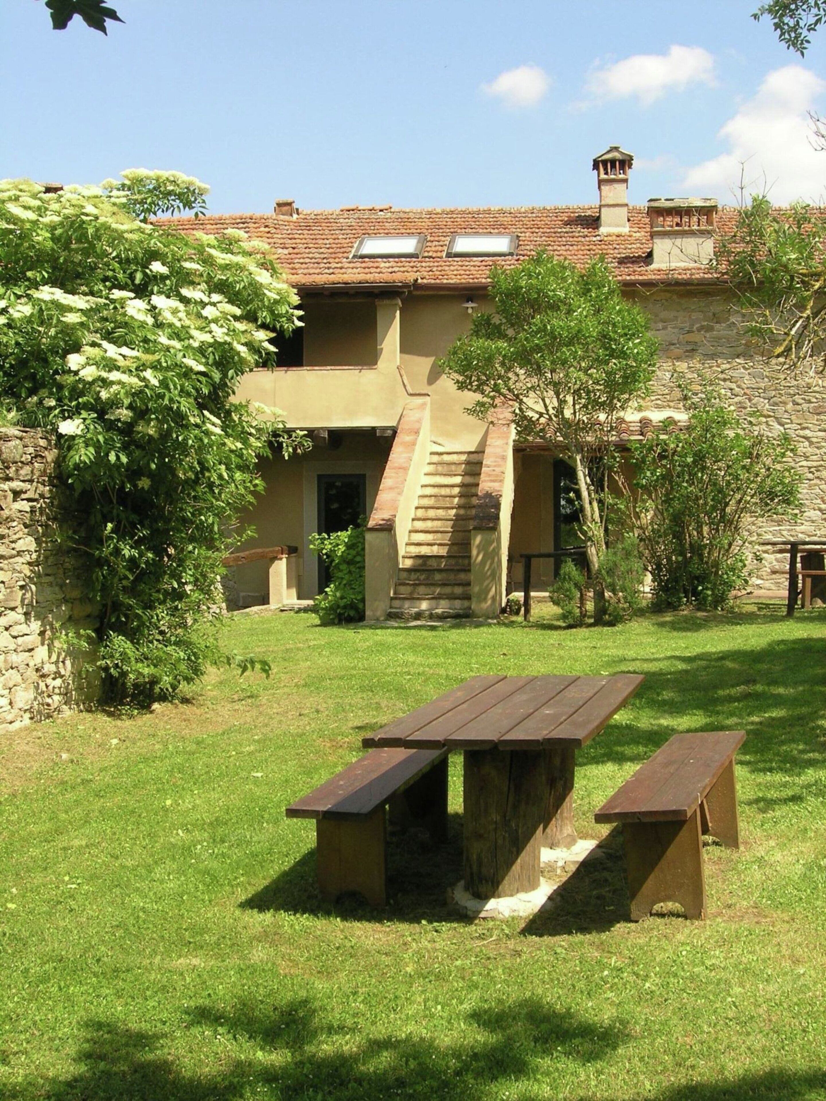 A rustic building with a stone facade, a wooden staircase, and a picnic table in the foreground.