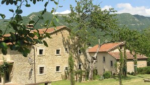 A stone building with a tiled roof, surrounded by a grassy area and trees, with mountains in the background. - Comfy Home in San Godenzo With Lake Nearby (San Godenzo)