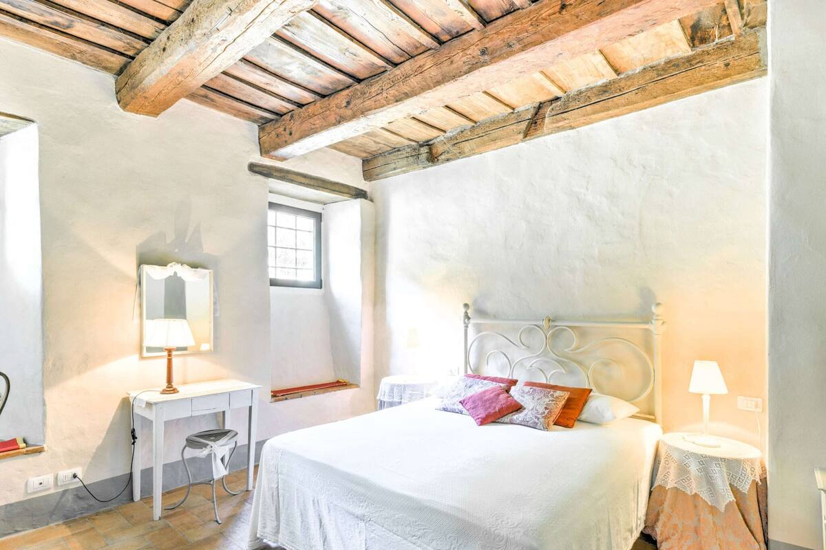 A bedroom with a bed, a desk, a chair, a window, and a lamp.