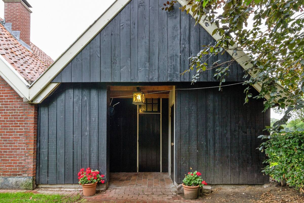 A dark wooden barn with a brick entrance and two potted plants with red flowers.