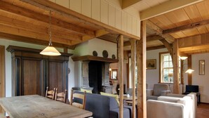 Een rustiek interieur met een houten eettafel, stoelen, een bank en een open haard.