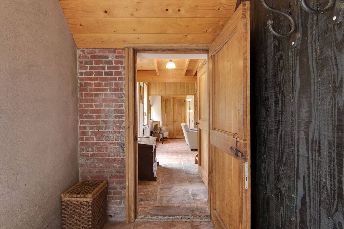A wooden hallway with a brick wall and a large wooden door.