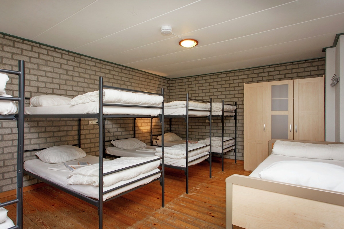 A dormitory room with bunk beds, a wooden wardrobe, and a brick wall.